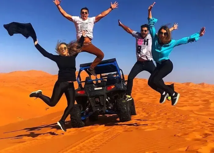 Travelers jumping beside a quad bike on orange dunes